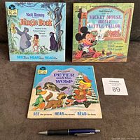 Three Walt Disney read along books with their matching records: The Jungle Book, Peter and the Wolf, Mickey Mouse Brave Little Tailor. Books show minor wear and writing marks. Includes pen for scale.