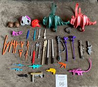 Full lot of 40 assorted vintage 1980's action figure weapons and accessories laid out, including helmets, swords, guns, and saddles.