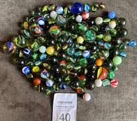 Lot of about 100 assorted vintage marbles spread out, showing a variety of colors and sizes.