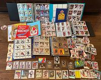 Wide shot showing two binders, loose cards, two green sealed boxes, collector album and hockey coaster on floor.