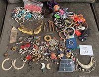 Full view of the lot showing a variety of colorful necklaces, bracelets, brooches, rings, earrings, and two silver pieces on a dark surface.