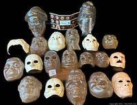 Overview photo showing all 24 soft vinyl masks arranged in four rows on black background. Masks display various expressions and sculptural features; a leaflet of instructions is placed in center-top.