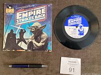 Photo showing The Empire Strikes Back read along book cover with Yoda image and the accompanying 7-inch vinyl record laid beside a pen for scale.