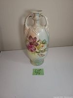 Front view of the antique oval porcelain vase showing hand-painted floral designs and relief handles.