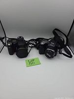Two cameras photographed against a white backdrop with Lot 50 label. Nikon film SLR camera on left, Kodak video camera on right.