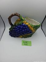 Front angled view showing the blue grapes, leaves, and brown handle of the ceramic jug