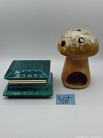 Photo showing green glazed vintage hinged lidded trinket dish next to a brown ceramic mushroom tealight holder with a hollow base, both items are positioned on a plain white background.