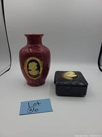 Photo showing the red ceramic vase with cameo medallion next to the black marbled trinket dish with lid and cameo medallion from an angle.