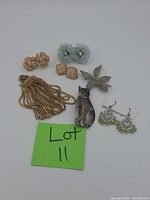 Photo showing vintage costume jewelry including bracelet, various earrings, and brooches arranged with a 'Lot 11' note.