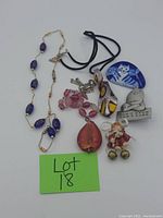 Photo of vintage costume jewelry lot including two necklaces and five decorative brooches arranged on a white background with a green 'Lot 18' card.