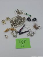 Photo showing vintage costume jewelry lot with a multi-strand pearl-style bracelet, dark purple beaded necklace, and various pairs of earrings with floral, bow, rhinestone, and pearl designs.