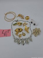 Display of vintage costume jewelry including gold and silver-tone brooches, earrings, rings, and a leaf design necklace with rhinestones.