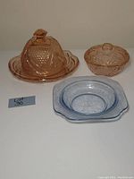 Front and top view of pink glass cheese and cracker plate with dome lid, pink trinket dish with lid, and blue salad bowl, showing patterns and shapes