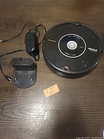 Overview of Roomba vacuum, charging station, and power adapter on wooden surface with lot number card.