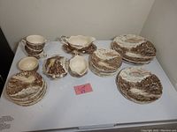 Full lot setup showing all plates, teacups, and serving pieces with countryside pattern in brown and cream hues