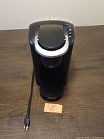 Front view of the black and silver Keurig coffee maker with power cord and drip tray visible