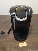 Front view of black Keurig K-Select coffee maker showing water reservoir and front drip tray with power cord.