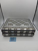Closed view of the rectangular stamped metal jewelry box showing floral and stripe patterns on top and sides.
