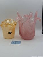 Two Murano style art glass vases side by side. Left is a yellow vase with ruffled clear-edged top and a label confirming Made in Italy. Right is a taller peach-colored vase with multiple clear-tipped ornamental projections on the top edge and a swirling pattern in the glass.