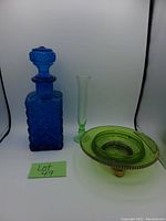 Blue glass decanter, clear slender vase, and green glass footed trinket dish shown together against white backdrop.