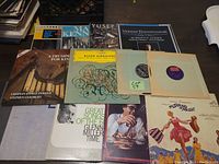 Photo showing various vintage vinyl LP albums including classical, jazz, and musical albums arranged on a dark surface.