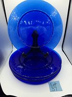 Photo of 6 stacked cobalt blue glass dinner plates with one plate displayed vertically on a stand.