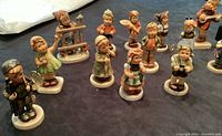 Photo showing 18 Hummel figurines on dark fabric surface, displaying various children figurines in different poses and outfits.