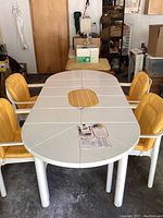 Oval white plastic patio table with two leaves and umbrella hole, surrounded by four yellow and white striped cushioned chairs.
