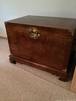 Front view of wooden trunk showing burl veneer surface, lid, brass circular front handle and corner guards