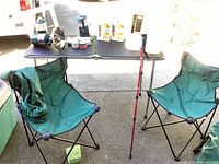 Two green fold-up camping chairs with mesh cup holders and black metal frames seen next to a folding table outdoors