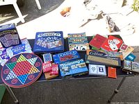 Photo of various boxed board games including Rummy-O, Dominoes, Cribbage board, Chinese Checkers, and playing card decks arranged on a table.