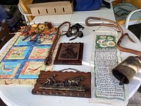 Group photo showing all wall hanging items on a white table including quilt, wooden plaques, cowbell, and floral decor