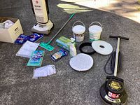Full lot showing the Oreck Orbiter floor cleaner, Hoover vacuum, cleaning pads, cleaning solutions, Swiffer mop, hand wipes, vacuum bags, belt, and manuals laid out on concrete.