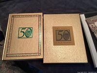 Two boxes of The Hobbit 50th Anniversary Special Edition, one box with green and gold design, slipcase with gold textured cover and title