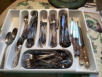 Tray organizer filled with Stanley Roberts stainless steel flatware including forks, spoons, knives, and 6 Outset steak knives with wooden handles on the side