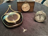 Three vintage clocks displayed on a dark surface: the German hanging clock, Diehl wooden clock, and Westclox Big Ben alarm clock with winding key placed in front.