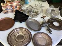 Wide view of all metal cake molds, fruit stand, pie cover, meat grinder, trays, and baking pans on white table