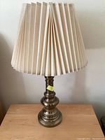 Two brass bedside lamps with pleated beige lampshades shown unlit on a wooden surface.