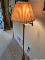 Brass swivel floor lamp with pleated fabric shade, lit and showing warm light.