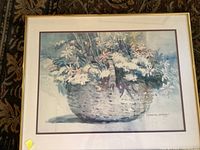 Framed print of a basket of flowers rendered in watercolor style in blue and white tones, set against a neutral background.