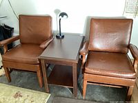 Two brown leather armchairs flanking a wooden side table with lamp on top
