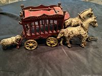 Side angle of the Overland Circus red cast iron cage pulled by two white spotted horses with harnesses and a small white bear following behind.