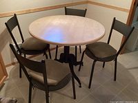 Full view of round wood tabletop with four black metal chairs around it, each with gray seat cushion