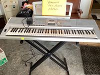 Full view of Yamaha DGX-205 digital piano on adjustable X-style stand with power adapter on top.