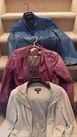 Three Danier leather jackets displayed hanging on a staircase, showing different colors and styles.