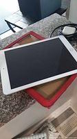 Apple iPad placed on top of a red cover showing the front screen and home button, lying on a granite counter.