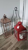 Three lanterns grouped on the floor: red, copper colored, and black metal hurricane style.