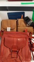 Red leather shoulder bag in front, tan waist pouch with black strap and blue wallet in background
