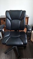 Front view of the black office chair showing padded backrest and seat with some contour lines.