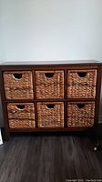 Front view of wooden storage cabinet with six woven wicker baskets in cubbies.